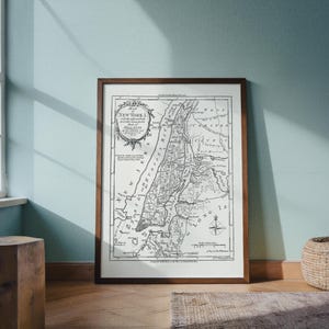 May include: A framed black and white map of New York City, with the title "Map New York I" at the top. The map is in a dark brown wooden frame, and is displayed on a light blue wall. The map shows the city's streets and waterways.