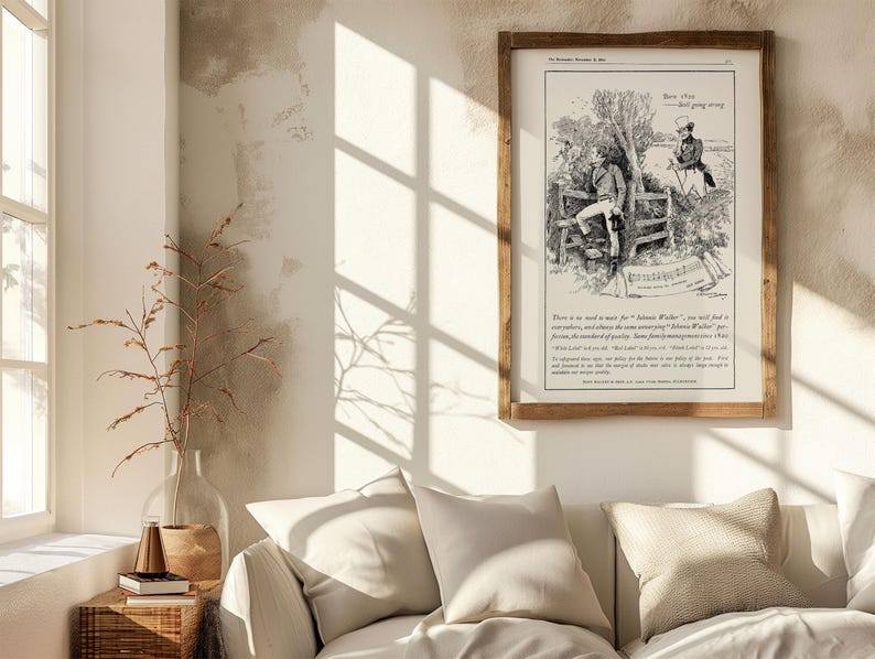 May include: A framed vintage illustration in a wooden frame. The black and white artwork depicts two men in a rural setting, with text below. The frame is rectangular and hangs on a neutral-colored wall, above a white sofa.