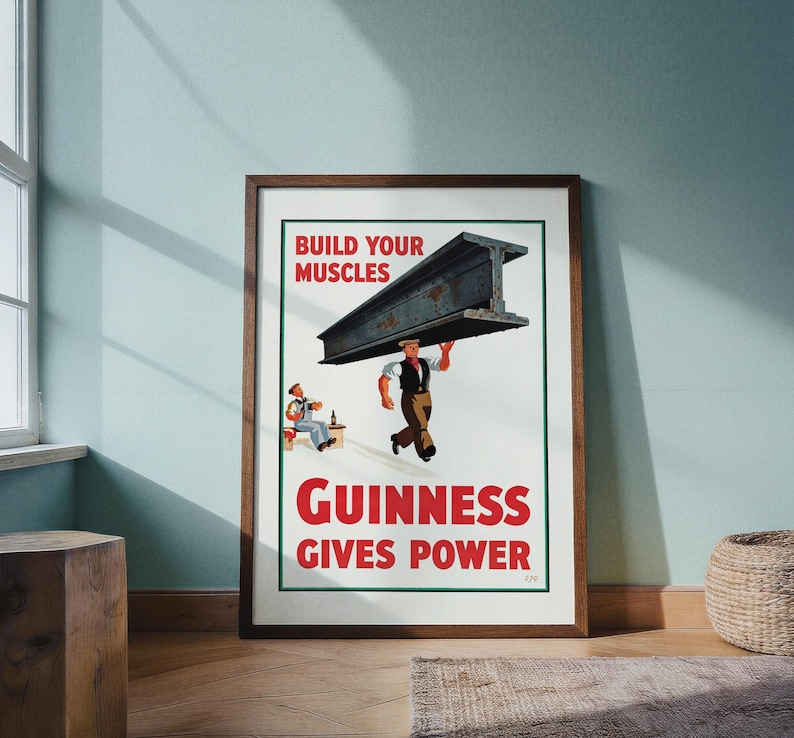 May include: A framed vintage Guinness advertisement. The poster features a man carrying a large steel beam with the text "BUILD YOUR MUSCLES" above and "GUINNESS GIVES POWER" below. A second man is seated, drinking.