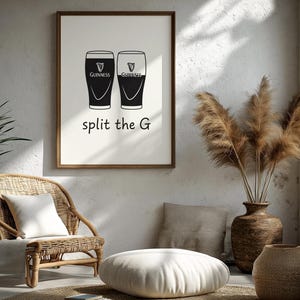 May include: A framed print featuring two Guinness pint glasses in black and white. The text "split the G" is below the glasses. The print is displayed in a room with a wicker chair, a floor cushion, and decorative plants.