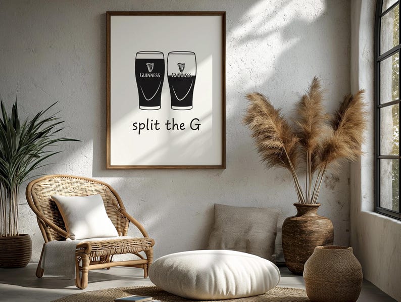 May include: A framed print featuring two Guinness pint glasses in black and white. The text "split the G" is below the glasses. The print is displayed in a room with a wicker chair, a floor cushion, and decorative plants.