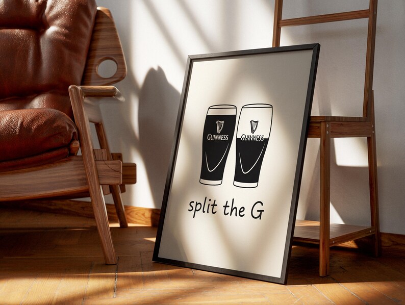 May include: Black and white framed print featuring two Guinness pint glasses with the text "split the G". The print is leaning against a wall, with a wooden chair and shelf in the background.