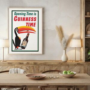Puede incluir: P&oacute;ster vintage enmarcado de Guinness con un tuc&aacute;n sosteniendo una botella de Guinness. El texto dice "Opening Time is Guinness Time" en rojo y verde. El tuc&aacute;n tiene un pico amarillo y rojo. El p&oacute;ster est&aacute; en un comedor.