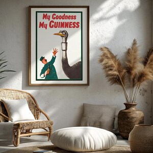 May include: A framed vintage Guinness advertisement featuring an illustration of a man in a green uniform offering a bottle to a tall ostrich. The text "My Goodness My Guinness" is displayed in red. The artwork is in a room with a wicker chair and decorative vase.