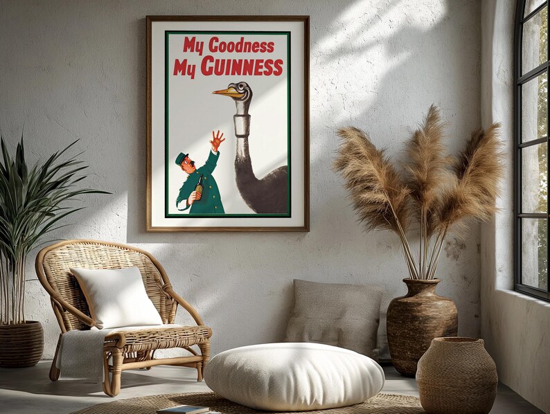 May include: A framed vintage Guinness advertisement featuring an illustration of a man in a green uniform offering a bottle to a tall ostrich. The text "My Goodness My Guinness" is displayed in red. The artwork is in a room with a wicker chair and decorative vase.