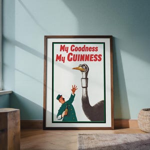 May include: Framed vintage Guinness advertisement featuring a cartoon ostrich with a long neck and a man in a green uniform. The text "My Goodness My Guinness" is in red and white. The artwork is in a wooden frame.