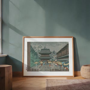 Puede incluir: Impresión enmarcada de un grabado en madera japonés que representa una escena de templo y calle. La obra de arte presenta una pagoda, edificios y figuras con paraguas. La paleta de colores incluye verdes, marrones y tonos apagados.