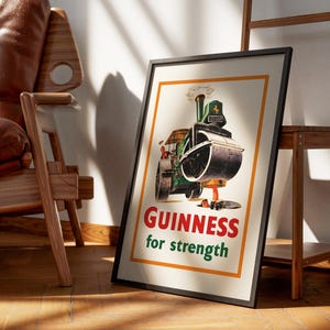 May include: Framed vintage Guinness advert poster. The poster shows a green and black steamroller with the words "Guinness for strength" in red and green. The poster is in a black frame and leans against a wall.