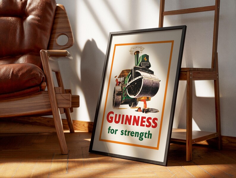 May include: Framed vintage Guinness advert poster. The poster shows a green and black steamroller with the words "Guinness for strength" in red and green. The poster is in a black frame and leans against a wall.