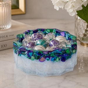 May include: A faceted, octagonal resin bowl filled with round, foil-wrapped candies. The bowl features a gradient design with a translucent, frosted white base that transitions into a vibrant rim embedded with deep blue and green crushed shell fragments.