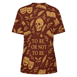 May include: A short-sleeve t-shirt in a deep reddish-brown color featuring a repeating pattern of skulls, open books, theater masks, and quill pens. The text "TO BE, OR NOT TO BE" is printed in large, bold, light-colored letters on the center front.