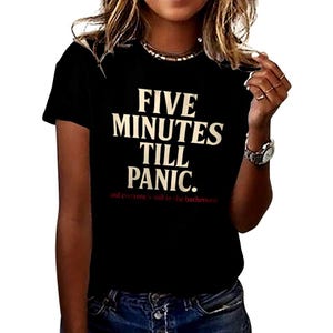 May include: Black t-shirt with the text "FIVE MINUTES TILL PANIC." in white, and the text "and everyone's still in the bathroom" in red. The shirt has short sleeves and a crew neck.