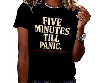 May include: Black t-shirt with the text "FIVE MINUTES TILL PANIC." in white, and the text "and everyone's still in the bathroom" in red. The shirt has short sleeves and a crew neck.