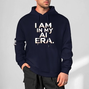 May include: Navy blue hoodie with the text "I AM IN MY AI ERA." in a white and light orange gradient. The hoodie has a drawstring hood and a small logo on the left sleeve.
