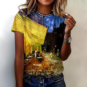 May include: Short-sleeved t-shirt featuring a print of Vincent van Gogh's "Cafe Terrace at Night." The artwork depicts a yellow-lit cafe with patrons, a starry night sky, and the artist's signature. The shirt has a round neckline and is made of a soft material.