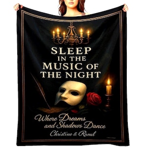 Puede incluir: Manta negra con el texto "SLEEP IN THE MUSIC OF THE NIGHT", una lámpara de araña, una máscara, una rosa roja y una vela. La manta también incluye el texto "Where Dreams and Shadows Dance Christine & Raoul."