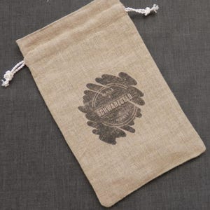 Peut inclure: Un sac à cordon beige en toile de jute avec un tampon noir qui dit "SCHWARZGOLD MONEY".