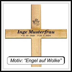 May include: A wooden cross with a small angel design at the top. The cross is engraved with the name "Inge Musterfrau" and the dates "8. 10. 1948 + 16. 3. 2024". Below the cross is a small plaque with the text "Motiv: &ldquo;Engel auf Wolke&rdquo;"