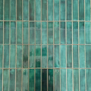 Puede incluir: Una superficie de pared cubierta con azulejos de cerámica rectangulares dispuestos en un patrón de colocación vertical. Cada azulejo presenta un esmalte brillante en tonos verde azulado y esmeralda con sutiles variaciones y juntas finas.
