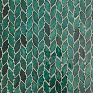 May include: A wall covering composed of numerous elongated diamond-shaped tiles in varying shades of deep emerald and forest green. Each individual tile features a glossy, reflective surface and is outlined by thin, light-colored grout lines.
