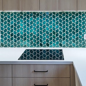 Può includere: Un piano di lavoro da cucina con un backsplash in mosaico di piastrelle blu turchese con un motivo a foglia. Il piano di lavoro ha un piano cottura elettrico nero e armadi bianchi.