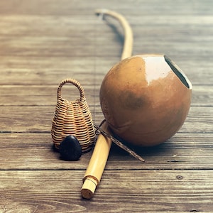 May include: A set of three traditional Brazilian musical instruments: a berimbau, a cabasa, and a pandeiro. The berimbau is a single-string musical bow, the cabasa is a gourd rattle, and the pandeiro is a frame drum.