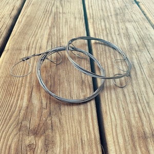 May include: A close-up of three silver wire rings on a wooden surface. The rings are intertwined and appear to be made of thin, flexible wire.