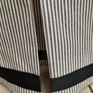 May include: Close-up of the bottom edge of a white and black striped fabric skirt with a black ribbon trim.