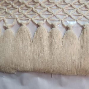 May include: Cream-coloured decorative trim with a woven top section and diamond pattern, and a row of tassels. The tassels hang below the woven section, creating a textured, elegant look. Suitable for home decor projects.