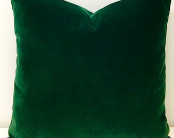 May include: A deep green velvet pillow with a smooth, soft texture. The pillow is square and has a simple, elegant design.