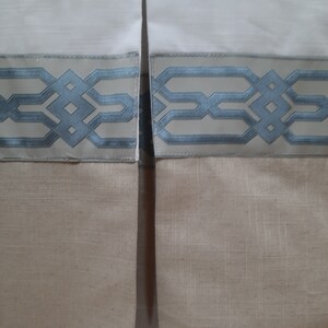May include: Close-up of a white bed skirt with a blue and white geometric patterned trim. The skirt is made of a linen fabric and has a gathered look.