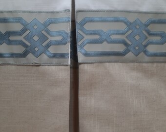 May include: Close-up of a white bed skirt with a blue and white geometric patterned trim. The skirt is made of a linen fabric and has a gathered look.