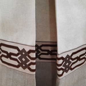 May include: Close-up of the bottom of a pair of beige linen curtains with a brown geometric patterned trim.