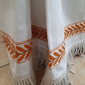 Pode incluir: Cortina de chuveiro branca com design de folhas laranja e cinza e acabamento em franjas brancas.