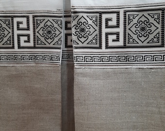 May include: Two white curtains with a black and gray geometric patterned trim. The curtains are made of a textured fabric.