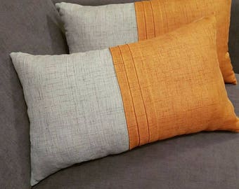 May include: Two rectangular throw pillows on a gray sofa. Each pillow has a two-tone design: one side is light gray, and the other is orange with vertical stitched details. The pillows add a decorative touch to the living room.