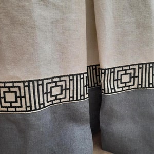 Pode incluir: Dois painéis de tecido branco transparente com uma borda inferior cinza e um padrão geométrico preto e branco ao longo da borda superior.