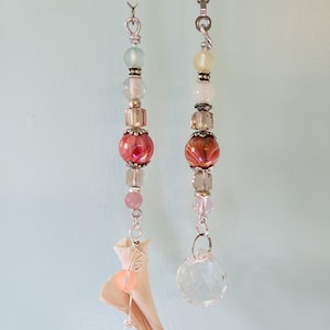 May include: Two decorative ceiling fan pull chains with beads and crystals. One chain has a pink and white shell with a clear crystal at the bottom. The other chain has a clear crystal at the bottom.