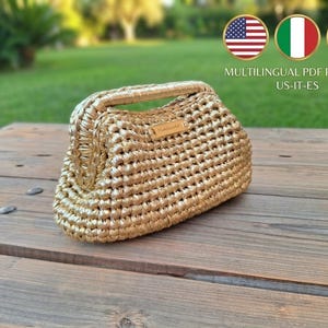 May include: A gold-colored crocheted handbag with a structured frame closure and a small rectangular label on the front. The bag features a dense, textured stitch pattern and a metallic finish, presented as a multilingual PDF pattern.