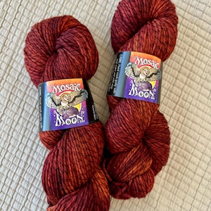 May include: Two skeins of red and orange variegated yarn. Each skein has a label with the text "Mosaic Moon" and an illustration of an owl. The yarn is a bulky weight and appears soft.