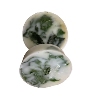 May include: Two round, white soap bars with green swirls. The soap bars are stacked on top of each other.