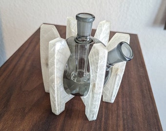 May include: A clear glass water pipe with a gray base and a white plastic stand. The stand has a geometric design with multiple points.