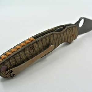 May include: A brown and tan pocket knife with a partially open blade. The handle has a textured pattern and a copper-colored accent.
