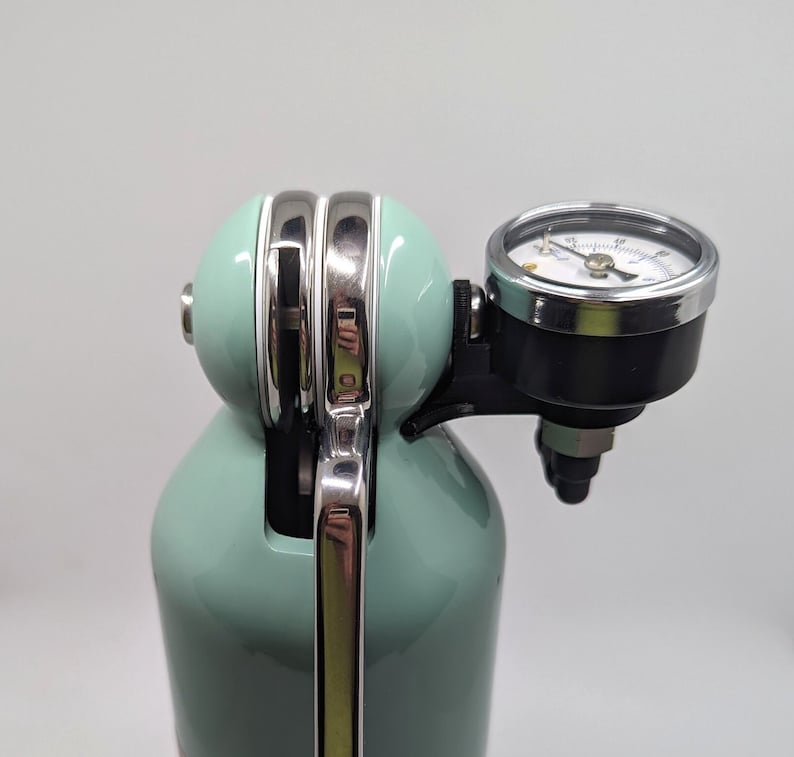 Pode incluir: Um sif&atilde;o de soda verde menta com uma pega cromada e um man&oacute;metro. O man&oacute;metro tem um mostrador preto com marcas brancas e uma agulha prateada.