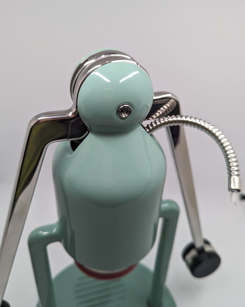 Pode incluir: Uma cafeteira azul claro e prateada com uma mangueira longa e flex&iacute;vel. A cafeteira tem uma parte superior redonda e bulbosa e uma base com um padr&atilde;o de grade.