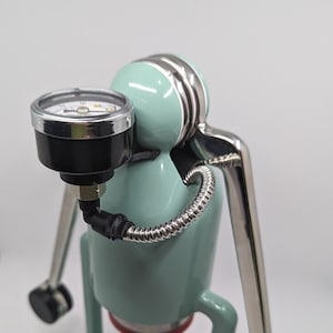 Pode incluir: Uma m&aacute;quina de caf&eacute; espresso verde menta com uma alavanca prateada e um man&ocirc;metro. O man&ocirc;metro est&aacute; conectado a uma mangueira preta que envolve a m&aacute;quina.