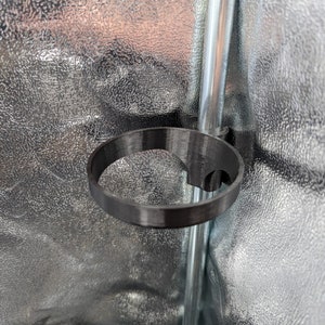 May include: A black plastic cup holder attached to a silver pole. The cup holder is designed to hold a beverage can or bottle.