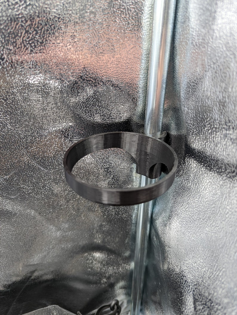 May include: A black plastic cup holder attached to a silver pole. The cup holder is designed to hold a beverage can or bottle.