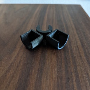 May include: Three black plastic connectors for joining pipes or tubing. The connectors are shaped like a 'U' and have a square opening on each side.