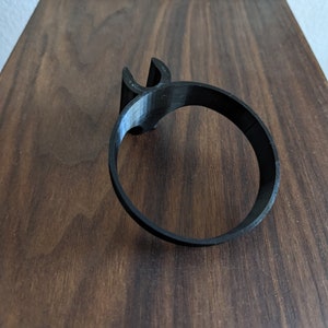 May include: A black plastic cup holder with a simple design. The holder is designed to fit around a standard-sized cup.